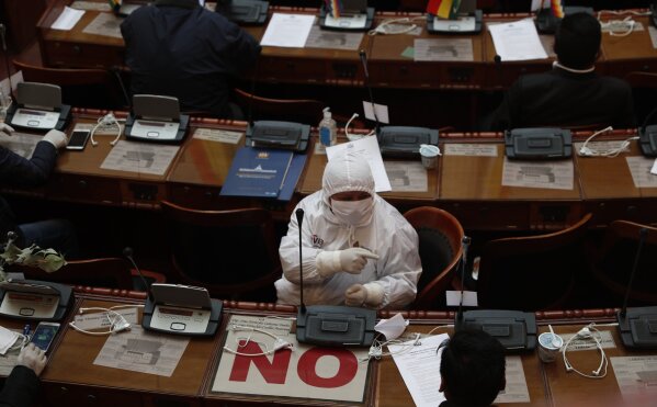 A lawmaker wearing protective gear attends a session at Congress' Plurinational Legislative Assembly in La Paz, Bolivia, Friday, April 17, 2020. Amid the spread of the new coronavirus, other lawmakers are attending sessions virtually. The sign "no" is used by politicians who are opposition to the government of former President Evo Morales. (AP Photo/Juan Karita)