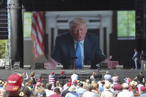 Former President Donald Trump addresses the crowd via video Saturday, June 12, 2021, at the River's Edge Apple River Concert Venue in New Richmond, Wis. The MAGA rally was organized by pillow salesman-turned conspiracy peddler Mike Lindell. For a few hours last weekend, thousands of Donald Trump’s loyal supporters came together under the blazing sun in a field in Western Wisconsin to live in an alternate reality where the former president was still in office — or would soon return. (AP Photo/Jill Colvin)
