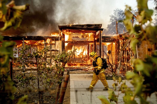 FILE - Woodbridge firefighter Joe Zurilgen passes a burning home as the Kincade Fire rages in Healdsburg, Calif., on Oct. 27, 2019. California Insurance Commissioner Ricardo Lara announced plans on Thursday, Sept. 21, 2023, aimed at keeping home insurers in California amid increasing risks from climate change. (AP Photo/Noah Berger, File)