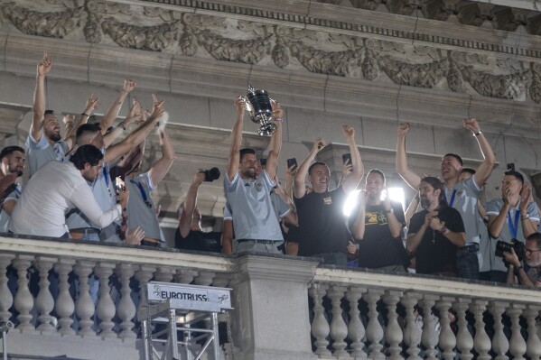 Novak Djokovic, center, holds the U.S. Open trophy in his hands as he makes a surprise appearance on the balcony of Belgrade's city hall during a celebration for members of the Serbian national basketball team in Belgrade, Serbia, Tuesday, Sept. 12, 2023. Thousands of fans gathered in the Serbian capital on Tuesday to celebrate the country's national basketball team winning the silver medal at the FIBA World Cup. (AP Photo/Marko Drobnjakovic)