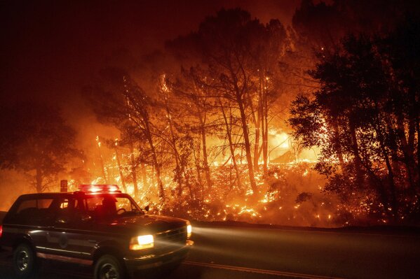A fire vehicle passes burning trees on Pleasants Valley Rd. near Winters, Calif., as the LNU Lightning Complex fires tear through the area on Wednesday, Aug. 19, 2020. Fire crews across the region scrambled to contain dozens of wildfires sparked by lightning strikes as a statewide heat wave continues. (AP Photo/Noah Berger)