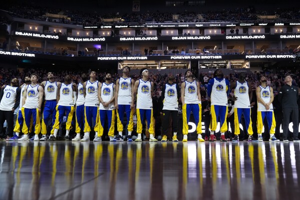The Golden State Warriors watch a video tribute to late assistant coach Dejan Milojevic, who died Jan. 17 after suffering a heart attack, before an NBA basketball game against the Atlanta Hawks, Wednesday, Jan. 24, 2024, in San Francisco. (AP Photo/Godofredo A. Vásquez)