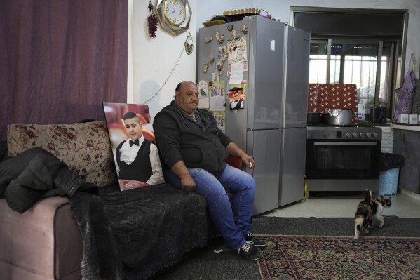 Ali Halhouli sits next to a photo of his slain son Rami Halhouli, in their house in Shuafat refugee camp in east Jerusalem, Sunday, March 17, 2024. Halhouli, 12, was shot by an Israeli police officer while launching a firework in the refugee camp on March 12. (AP Photo/Mahmoud Illean)