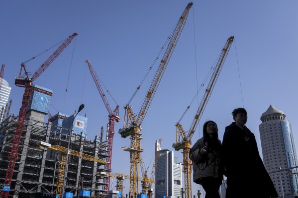 A young couple walk by a construction site near office buildings in the Central Business District in Beijing on March 2, 2024. China's efforts to restore confidence and rev up the economy will top the agenda during this month’s meeting of the ceremonial national legislature.(AP Photo/Andy Wong)