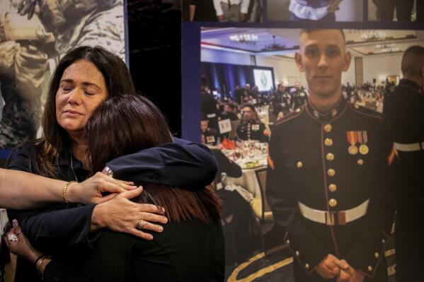 Christiana Sweetwood, mother of Marine Lance Corporal Chase Sweetwood, hand coming from left, Aleta Bath, mother of Private First Class Evan Bath and Lupita Garcia, mother of Marine Lance Corporal Marco Barranco embrace each other at a press conference next to a picture of Chase Sweetwood on Thursday, July 29, 2021, in Oceanside, Calif. The families of eight Marines and one sailor who died when their amphibious assault vehicle sank off the Southern California coast in the summer of 2020 plan to sue the manufacturer of the vehicle that resembles an armored seafaring tank, their lawyers announced Thursday. (Sam Hodgson/The San Diego Union-Tribune via AP)