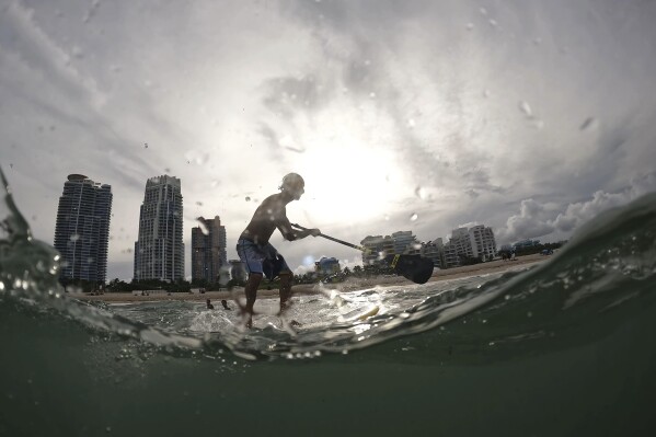 Graziano La Grasta, a local contractor and paddle board enthusiast, rides a small wave off South Beach, Friday, July 28, 2023, in Miami Beach, Fla. Humans naturally look to water for a chance to refresh, but when water temperatures get too high, some of the appeal is lost. (AP Photo/Rebecca Blackwell)