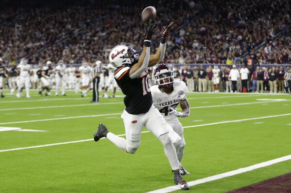 Oklahoma State wide receiver Rashod Owens, left, reaches for the ball on a touchdown reception in front of Texas A&M defensive back Kent Robinson during the second half of the Texas Bowl NCAA college football game Wednesday, Dec. 27, 2023, in Houston. (AP Photo/Michael Wyke)