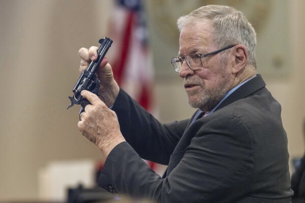 Lucien Haag, a witness on forensic science firearms evidence examination and shooting reconstruction, shows the jury a gun like the one used in rehearsal for the film 