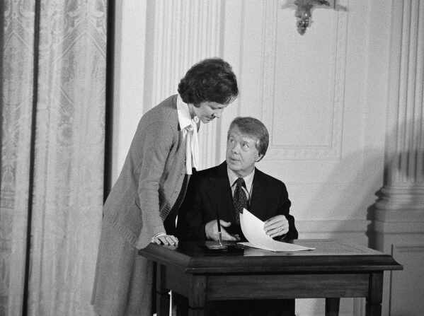 FILE - President Jimmy Carter speaks with his wife, first lady Rosalynn Carter, before signing an executive order establishing a Presidential Commission on Mental Health, February 17, 1977, in the East Room of the White House in Washington.  Health care experts say the advocacy of Rosalynn Carter, who died Sunday, Nov. 19, 2023, at the age of 96, created a framework for much of the progress on mental illness in America.  (AP Photo/Charles Tasnadi, file)