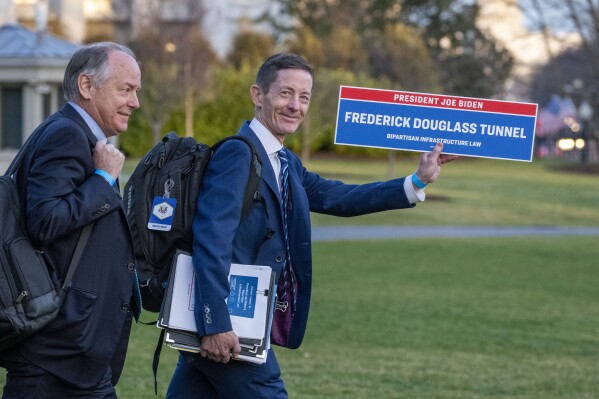 White House deputy chief of staff Bruce Reed, right, carries a sign as he walks to board Marine One upon departure on the South Lawn of the White House, Wednesday, March 1, 2023, in Washington. (AP Photo/Alex Brandon)