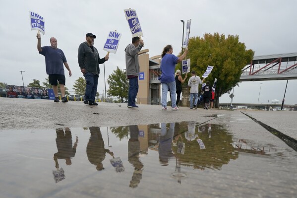 Picketers are reflected in a puddle as they strike outside of the General Motors assembly plant, Tuesday, Oct. 24, 2023, in Arlington, Texas. The United Auto Workers union is turning up the heat on General Motors as 5,000 workers walked off their jobs at the highly profitable SUV factory. (AP Photo/Julio Cortez)