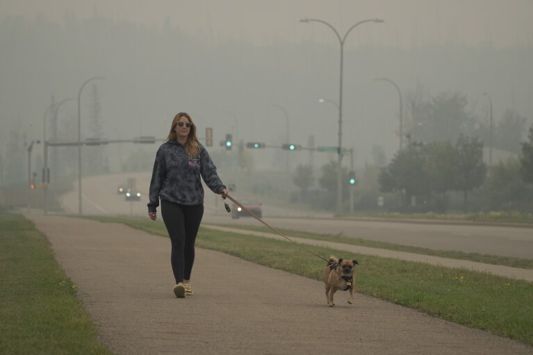 Brittnee McIsaac, a school teacher, walks her dog on a smoky day because of wildfires in Fort McMurray, Canada, on Saturday, Sep. 2, 2023. (AP Photo/Victor R. Caivano)