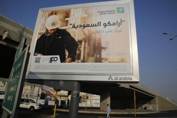 FILE - A man walks under a billboard displaying an advertisement for Saudi Arabia's state-owned oil giant Aramco with Arabic reading "Saudi Aramco, soon on stock exchange" in Jiddah, Saudi Arabia on Nov. 12, 2019. Oil giant Saudi Aramco said Sunday, May 15, 2022 its profits soared more than 80% in the first three months of the year, as the state-backed company cashes in on the volatility in global energy markets and soaring oil prices following Russia’s invasion of Ukraine. (AP Photo/Amr Nabil, File)