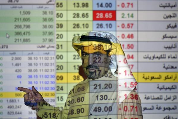 FILE- In this Dec. 12, 2019, file photo, a trader talks to others in front of a screen displaying Saudi stock market values at the Arab National Bank in Riyadh, Saudi Arabia. Saudi Aramco said Tuesday, May 4, 2021, it's profits soared by 30% for the first-quarter of the year, compared to last year, riding on the back of higher crude oil prices as some of the world's biggest economies claw their way out of recession and ease restrictions amid vaccine roll-outs against COVID-19.(AP Photo/Amr Nabil, File)