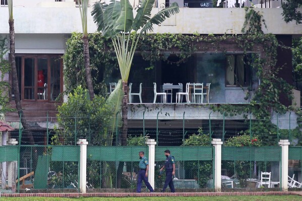FILE - Bangladeshi policemen walk past the Holey Artisan Bakery in Dhaka's Gulshan area, Bangladesh, one day after heavily armed militants held dozens of people hostage at the restaurant in a bloody 10-hour standoff, July 3, 2016. Bangladesh’s High Court has commuted the death sentences of seven Islamic militants to life in prison for their role in the attack on the cafe that killed 20 people, mostly foreigners. (AP Photo/File)