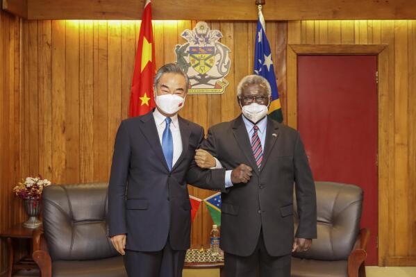 In this photo released by Xinhua News Agency, Solomon Islands Prime Minister Manasseh Sogavare at right lock arms with visiting Chinese Foreign Minister Wang Yi in Honiara, Solomon Islands, Thursday, May 26, 2022. (Xinhua via AP)