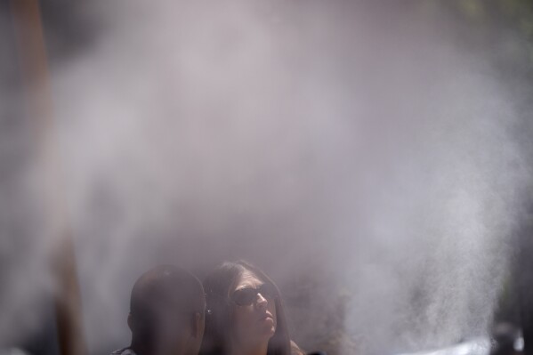 People cool off in misters along the Las Vegas Strip, Tuesday, June 4, 2024, in Las Vegas. Parts of California, Nevada and Arizona are expected to bake this week as the first heat wave of the season arrives with triple-digit temperatures. (AP Photo/John Locher)