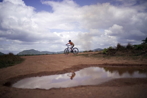 A youth rides a bicycle through Wowetta, in the Essequibo region, Guayana, Saturday, Nov. 18, 2023. Venezuela has long claimed the region — a territory larger than Greece and rich in oil and minerals. (AP Photo/Juan Pablo Arraez)