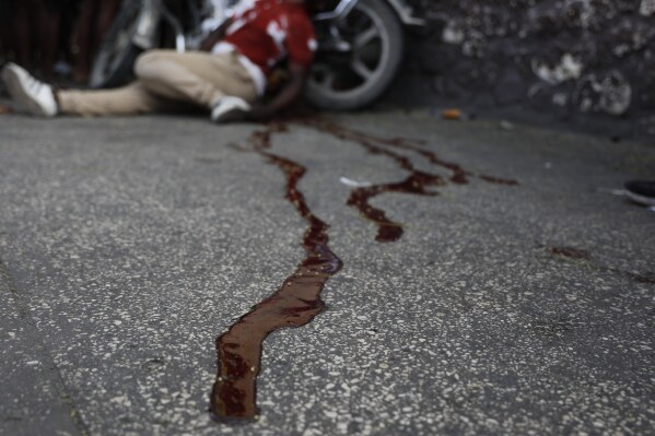 The body of a man lies in a pool of blood alongside his motorcycle, in the Delmas area of Port-au-Prince, Haiti, March 8, 2024. Witnesses say he was shot by two unidentified men on motorcycles. (AP Photo/Odelyn Joseph)