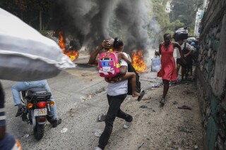 People walk past burning tires during a protest against Haitian Prime Minister Ariel Henry in Port-au-Prince, Haiti, Monday, Feb. 5, 2024. Banks, schools and government agencies closed in Haiti’s northern and southern regions on Monday while protesters blocked main routes with blazing tires and paralyzed public transportation, according to local media reports. (AP Photo/Odelyn Joseph)