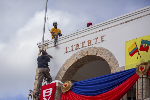 Workers hang decorations for a welcoming ceremony for Colombian President Gustavo Petro, in Jacmel, Haiti, Wednesday, Jan. 22, 2025. (AP Photo/Patrice Noel)