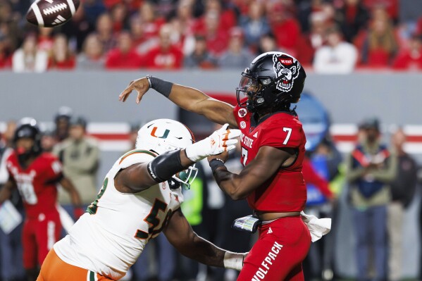 North Carolina State's MJ Morris (7) throws as he is hit by Miami's Branson Deen, left, during the first half of an NCAA college football game in Raleigh, N.C., Saturday, Nov. 4, 2023. (AP Photo/Ben McKeown)
