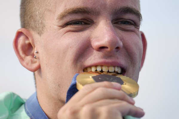 Gold medalist Hungary's Kristof Rasovszky bites down on his gold medal as he poses for photographers during the medal ceremony at the end of marathon swimming men's 10km competition at the 2024 Summer Olympics, Friday, Aug. 9, 2024, in Paris, France. (AP Photo/Vadim Ghirda)