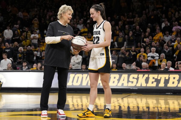 Iowa coach Lisa Bluder presents guard Caitlin Clark (22) with a commemorative basketball after the team's NCAA college basketball game against Michigan, Thursday, Feb. 15, 2024, in Iowa City, Iowa. Clark broke the NCAA women's career scoring record. (AP Photo/Matthew Putney)