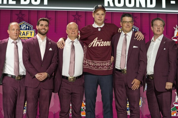 Daniil But poses with Arizona Coyotes officials after being picked by the team during the first round of the NHL hockey draft, June 28, 2023, in Nashville, Tenn. (AP Photo/George Walker IV, file)