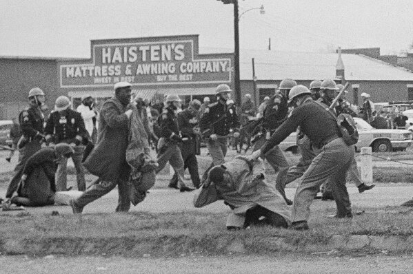 FILE - In this March 7, 1965, file photo, a state trooper swings a billy club at John Lewis, right foreground, chairman of the Student Nonviolent Coordinating Committee, to break up a civil rights voting march in Selma, Ala. The March 7, 2021, Selma Bridge Crossing Jubilee will be the first without the towering presence of Lewis, as well as the Rev. Joseph Lowery, the Rev. C.T. Vivian and attorney Bruce Boynton, who all died in 2020. (AP Photo/File)