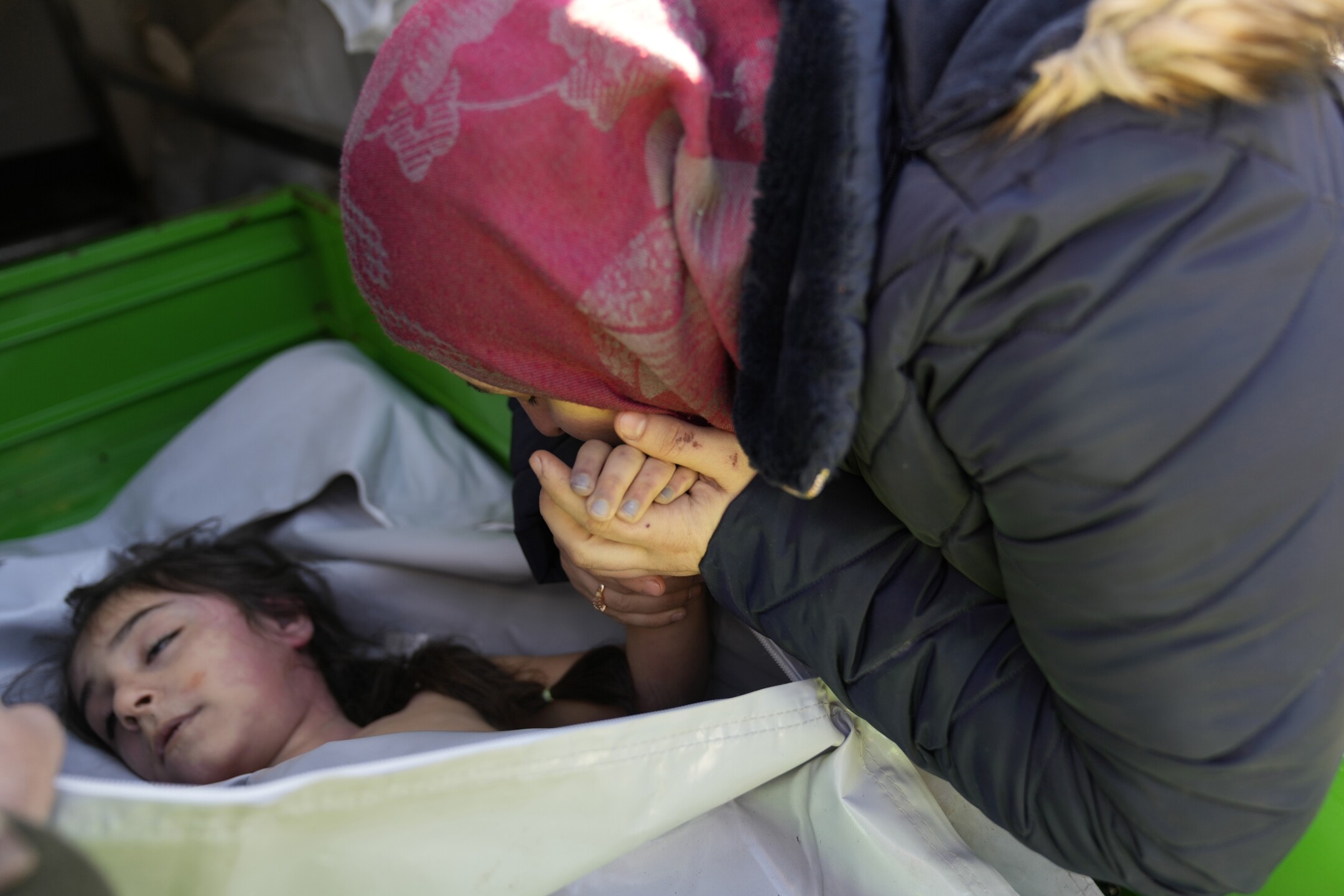A Syrian mother kisses the hand of her daughter, who was killed in a powerful earthquake that struck southern Turkey and Syria three days earlier, at the Turkish crossing point of Cilvegozu, in Reyhanli, southeastern Turkey, on the border of Syria, on Feb. 9, 2023. The girl's body will be transported to Syria for burial. (AP Photo/Hussein Malla)