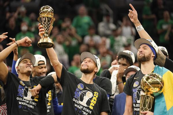 Golden State Warriors guard Stephen Curry, center, holds up the Bill Russell Trophy for most valuable player after the Warriors defeated the Boston Celtics in Game 6 to win basketball's NBA Finals championship, Thursday, June 16, 2022, in Boston. (AP Photo/Steven Senne)