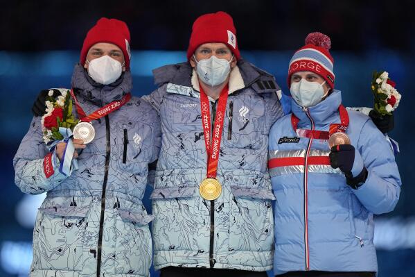 Gold medalist for the men's weather-shortened 50km mass start free cross-country skiing competition, Alexander Bolshunov, centre, of the Russian Olympic Committee stands with compatriot and silver medalist, Ivan Yakimushkin, left, and bronze medalist Simen Hegstad Krueger, right, of Norway on the podium during the closing ceremony of the 2022 Winter Olympics, Sunday, Feb. 20, 2022, in Beijing. (AP Photo/Jae C. Hong)