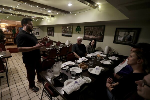 
              In this Friday, March 9, 2018 photo, Avital Food Tours culinary guide Philip Hall, left, speaks to a group taking the tour at Sotto Mare restaurant in San Francisco. Avital Tours runs excursions in San Francisco and Los Angeles that take diners to restaurants for progressive dinners, each course is served at a different restaurant. While inflation overall has been tame the past few years, many small businesses nonetheless have seen their costs rise, especially for labor and energy. (AP Photo/Jeff Chiu)
            