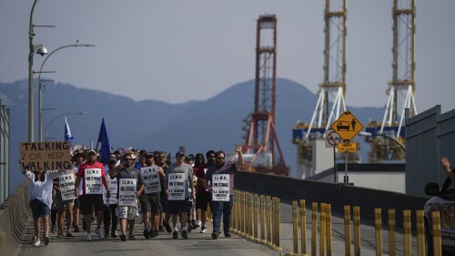 Striking International Longshore and Warehouse Union Canada workers march to a rally as gantry cranes used to load and unload cargo containers from ships sit idle at port, in Vancouver, on Thursday, July 6, 2023. (Darryl Dyck /The Canadian Press via AP)