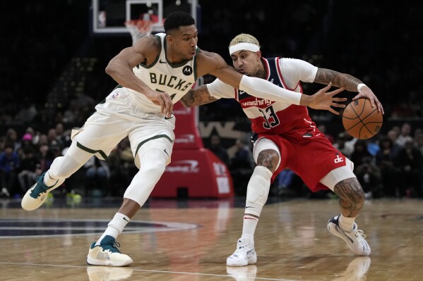 Milwaukee Bucks forward Giannis Antetokounmpo, left, reaches to knock the ball away from Washington Wizards forward Kyle Kuzma, right, during the second half of an NBA basketball game Monday, Nov. 20, 2023, in Washington. (AP Photo/Mark Schiefelbein)