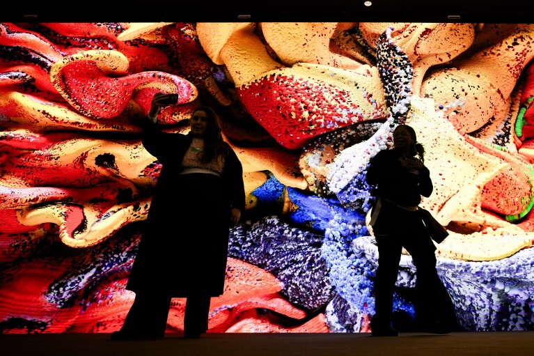 People gather in front of a screen with a artificial intelligence generated artwork by media artist Refik Anadol, inside the Congress Center where the Annual Meeting of World Economic Forum in Davos, Switzerland, Monday, Jan. 15, 2024. The annual meeting of the World Economic Forum is taking place in Davos from Jan. 15 until Jan. 19, 2024. (AP Photo/Markus Schreiber)
