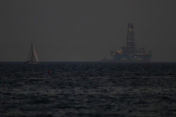FILE - An offshore drilling rig is seen in the waters off Cyprus' coastal city of Limassol, on July 5, 2020 as a sailboat sails in the foreground. The Cyprus government has given U.S. energy company Chevron another six months to come up with a revised plan to develop a sizeable natural gas deposit off the island nation's southern coastline after an earlier plan was deemed to lack a specific timetable, an official said Thursday, May 2, 2024. (AP Photo/Petros Karadjias, File)