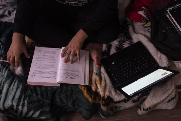 Deneffy Sánchez, 15, works on his homework with a school laptop on a bunk bed he shares with his mother and little sister in a studio apartment, where his family pays $700 a month to a roommate to rent the space, in Los Angeles, Saturday, Sept. 9, 2023. (AP Photo/Jae C. Hong)