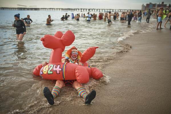 A clown lies on the beach as revelers enter the cold water during the annual Polar Bear Plunge, Monday, Jan. 1, 2024, in New York. (AP Photo/Andres Kudacki)