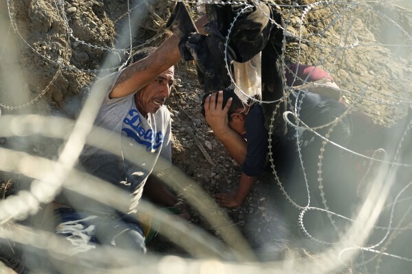 Migrantes que cruzaron el Río Bravo desde México a Estados Unidos pasan por debajo de un alambre con concertinas, o cuchillas pequeñas, el 22 de septiembre de 2023, en Eagle Pass, Texas. (AP Foto/Eric Gay)