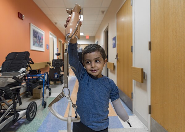 Four-year-old Omar Abu Kuwaik holds his new prosthetic arm in the air at Shriners Children's Hospital on Wednesday, Feb. 28, 2024, in Philadelphia. After his parents and sister were killed in an Israeli airstrike, Omar was pulled from the rubble and brought out of Gaza then to the United States, where he received treatment, including a prosthetic arm. He spent his days in a house run by a medical charity in New York City, accompanied by his aunt. (AP Photo/Peter K. Afriyie)