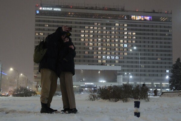 A couple take a selfie photo in front of a heart formed with lights switched on in hotel rooms during Valentine's Day in St. Petersburg, Russia, Wednesday, Feb. 14, 2024. (AP Photo/Dmitri Lovetsky)