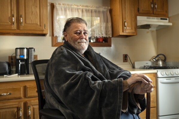 Russ Anderson wears a shawl to help keep warm at his home, Thursday, Oct. 19, 2023, in Waldoboro, Maine. Federal spending to help the poor stay warm may be reduced from last year, a cause for concern in cold-weather states. (AP Photo/Robert F. Bukaty)