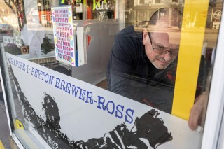 Peter Precourt levels a sign in the front window for the "There Goes My Hero: Chapter 1 Peyton Brewer-Ross" show Thursday, Feb. 8, 2024 at Art:Works on Main gallery in Winthrop, Maine. One of the 18 people killed in the deadliest mass shooting in Maine history is being remembered in art, including some of his own. An art exhibit this weekend paid tribute to Peyton Brewer-Ross, a Navy shipbuilder and father. (Joe Phelan/The Kennebec Journal via AP)
