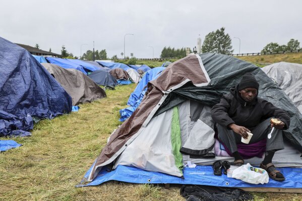 Kunau Eyumu Thierry sits outside his family tent at a camp on Tuesday, June 4, 2024, in Kent, Wash. Asylum seekers who have been looking for shelter in Washington state, mainly from Angola, Congo and Venezuela, have set up an encampment in a Seattle suburb. (Kevin Clark/The Seattle Times via AP)