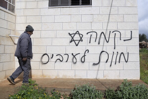 FILE - A man looks at graffiti that reads, in Hebrew, "revenge, death to Arabs," allegedly sprayed by Jewish West Bank settlers in the Palestinian West Bank village of Turmus Ayya, Feb. 18, 2024. The U.S. has imposed sanctions on a group of three extremist Israeli West Bank settlers who are accused of harassing and attacking Palestinians in an attempt to pressure them to leave their land. (AP Photo/Nasser Nasser, File)