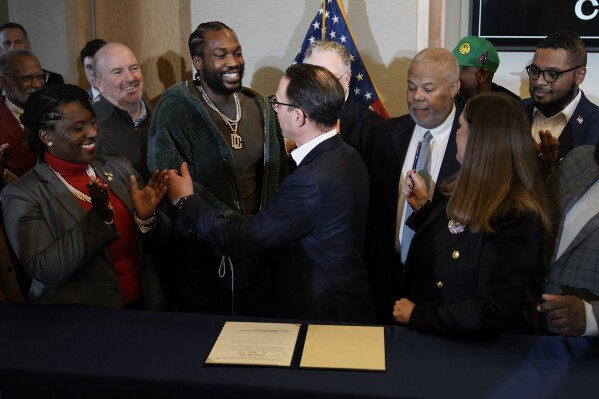 Rapper Meek Mill, center left, and Pennsylvania Gov. Josh Shapiro, center, move to embrace during a ceremonial bill signing in Philadelphia, Friday, Dec. 15, 2023. More criminal records in Pennsylvania can be sealed from public view and fewer people might be kept on probation or in county jails, under legislation signed by Gov. Josh Shapiro on Thursday. (AP Photo/Matt Rourke)