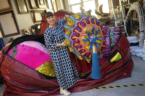 Portuguese artist Joana Vasconcelos poses for a picture while pulling one of her works out of a huge bag at her studio in Lisbon, Friday, Nov. 11, 2022. Vasconcelos has built her reputation over the past two decades. Her trademark features are large, flamboyant pieces that juxtapose the high brow and low brow, draw on Portuguese handicraft traditions, allude to women's rights, and possess a stealthy sense of humor. (AP Photo/Armando Franca)