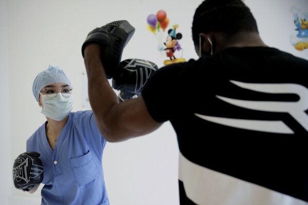 In this Wednesday, May 27, 2020 photo, medical worker Kenza, left, boxes during a training session with French boxer Hassan N’Dam at the Villeneuve-Saint-Georges hospital, outside Paris. A world champion French boxer is taking his skills to hospitals, coaching staff to thank the medical profession for saving his father-in-law from the virus, and giving them new confidence and relief from their stressful jobs. (AP Photo/Christophe Ena)